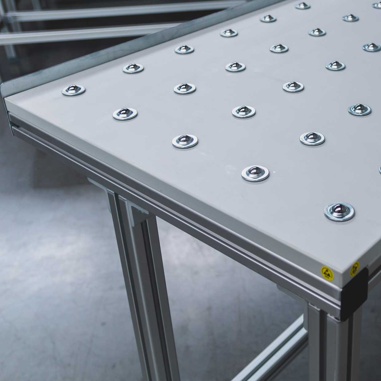 Blat stołu z osadzonymi, odpornymi na zużycie i tarcia kółkami, na ramie podstawy wykonanej z aluminiowych profili kwadratowych.