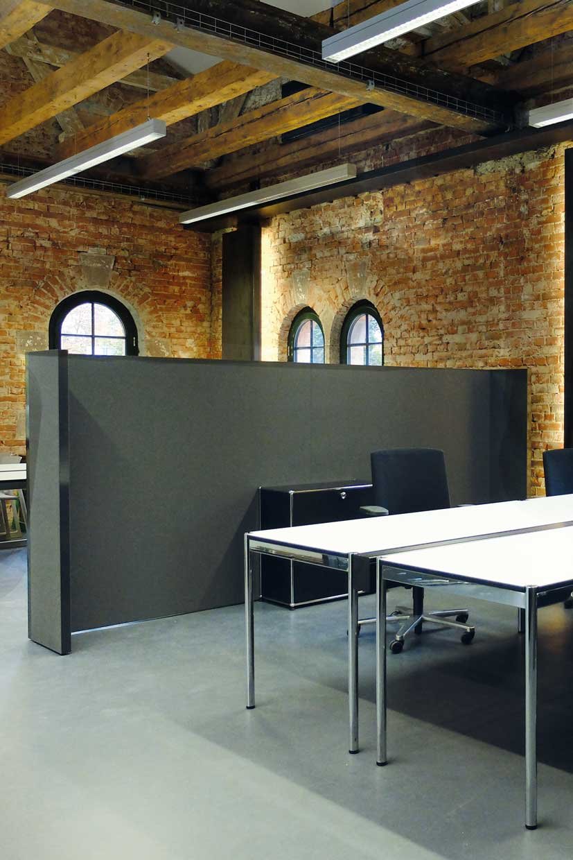 Large office space in which a partition wall covered with grey fabric separates two areas from each other