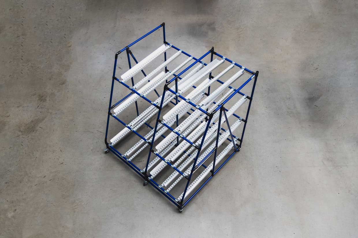A flow rack designed by BeeWaTec made of blue steel pipes with three levels and roller conveyors with side guides.